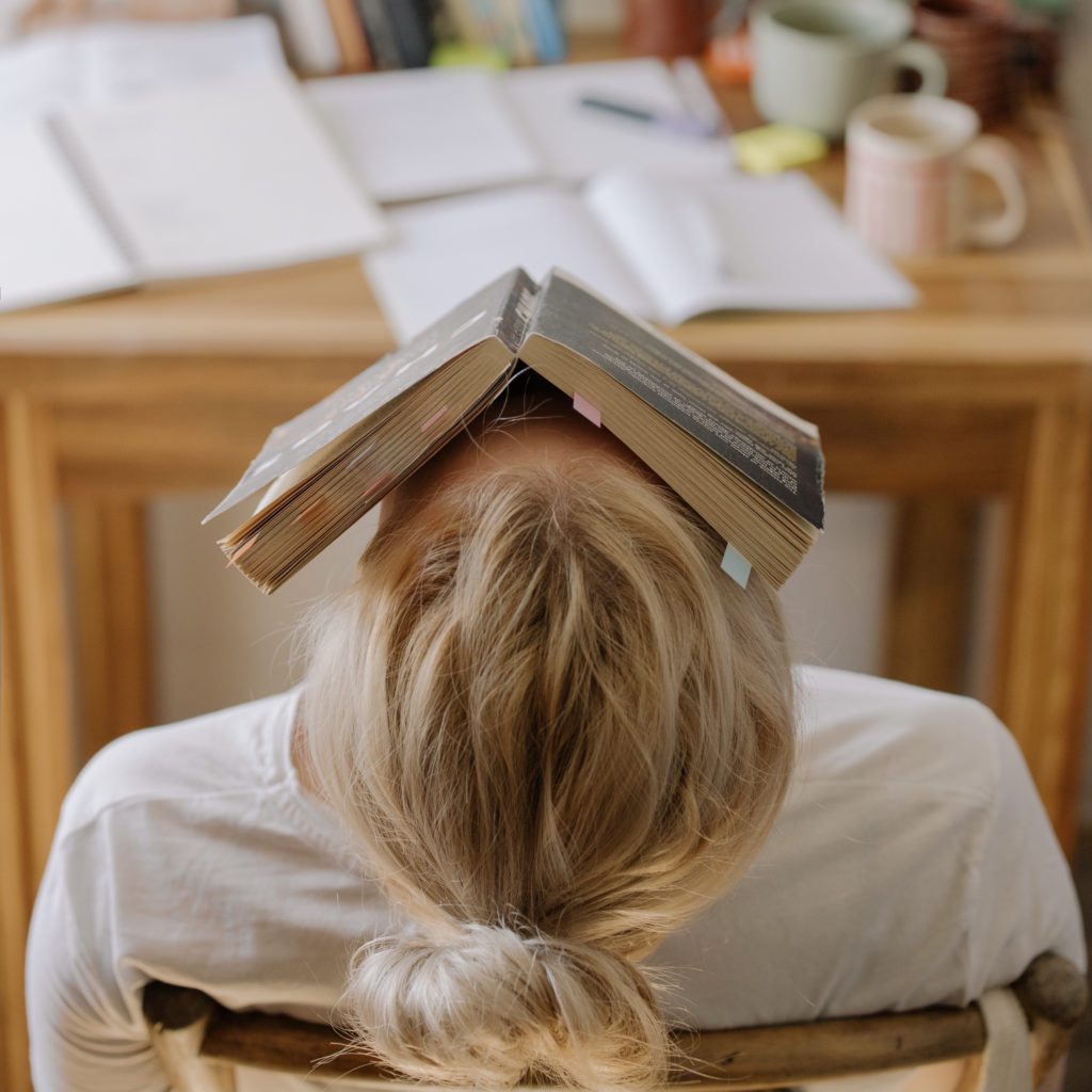 girl leaning back in her chair with her book open on her face. her desk is covered with papers | Parent College Student Contract | Positively Jane 