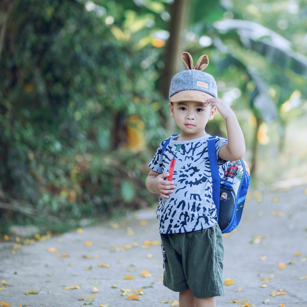 little boy standing on a path. His hat has ears sticking up and he is wearing a backpack |should kids receive an allowance | allowance for kids | Positively Jane