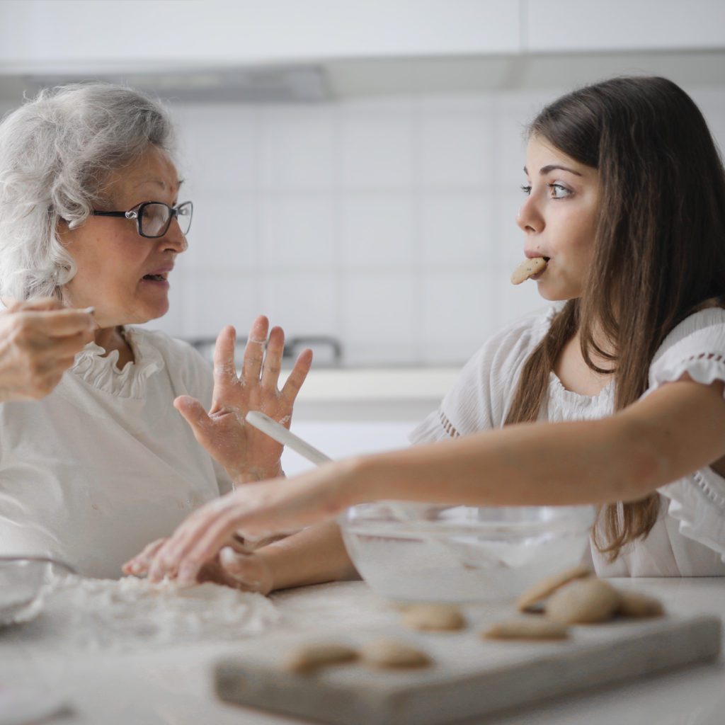 an older woman and a young girl making cookies. the young girl has one in her mouth | what makes a good house guest | Positively Jane  