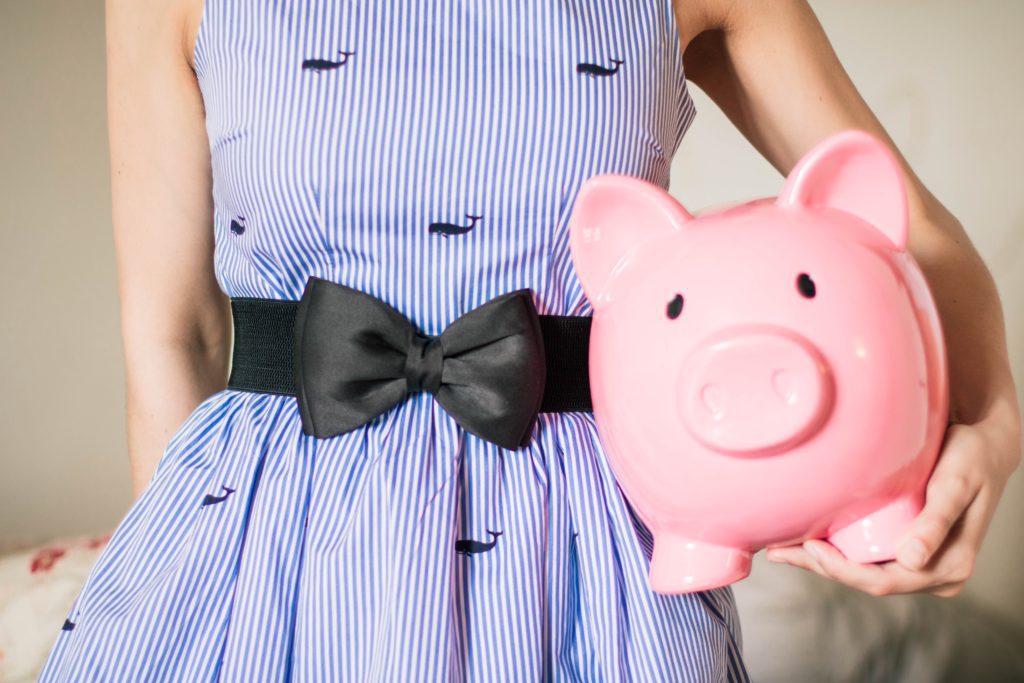 girl in a purple dress holding a pink piggy bank | budgeting for kids | should your children be on a budget | Positively Jane