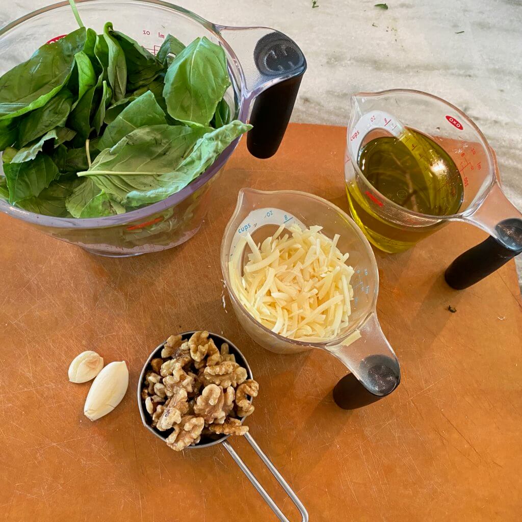 bowl of basil. measuring cups with olive oil, cheese and walnuts