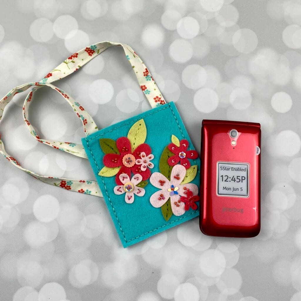 handmade felt phone case with flowers on it with the phone sitting next to it