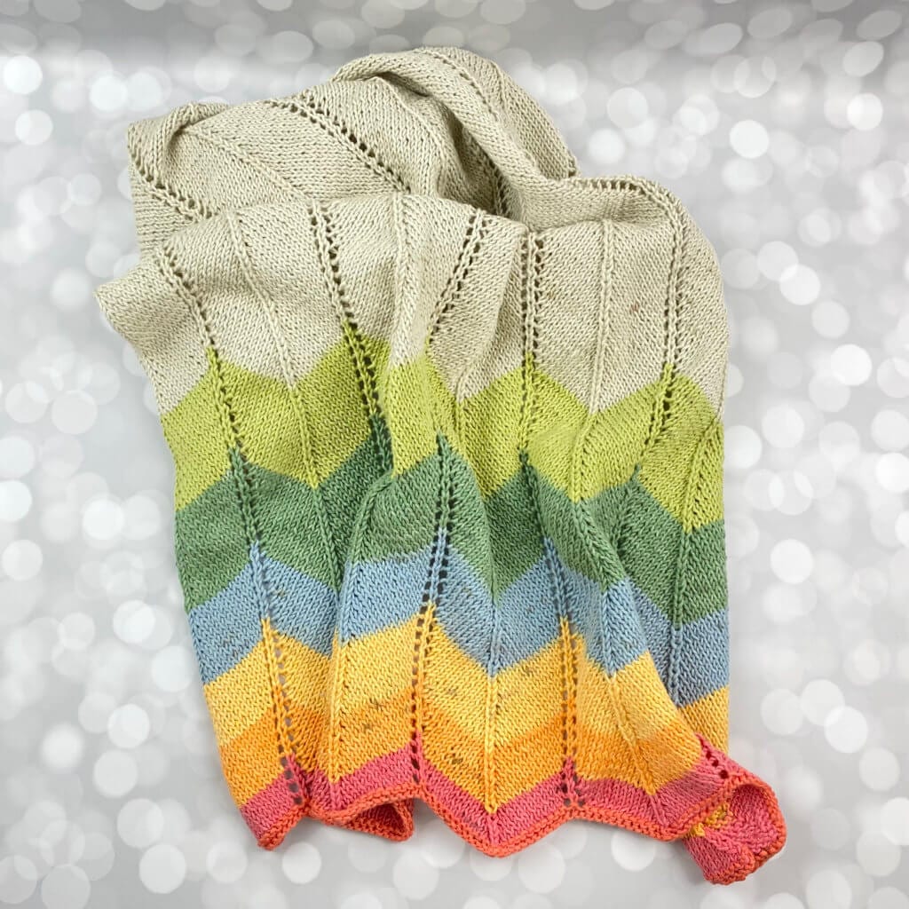 handmade knitted baby blanket with a colorful chevron pattern on the end - laying messily on a table