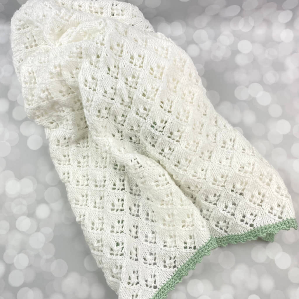handmade white baby blanket with lite green edging - laying messily on a table