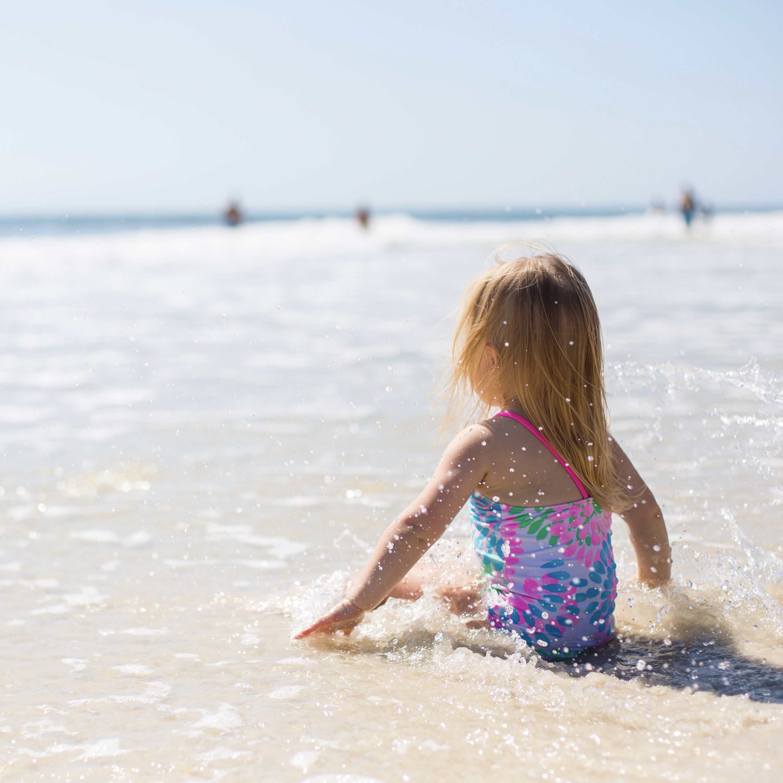 little girl sitting on the beach in her bathing suit