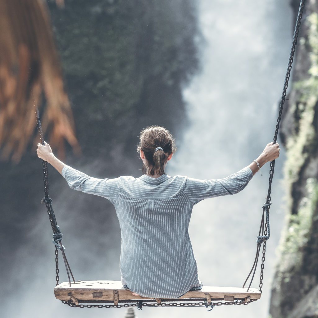 girl sitting on a large swing ovverlooking a waterfall. She appears to be high in the air | living a balanced life | Positively Jane