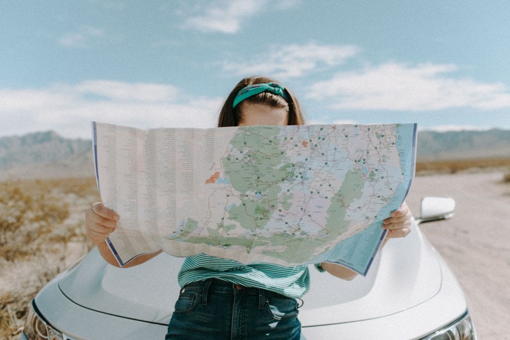 girl leaning against a car holding a large map that covers her face | purpose of a budget