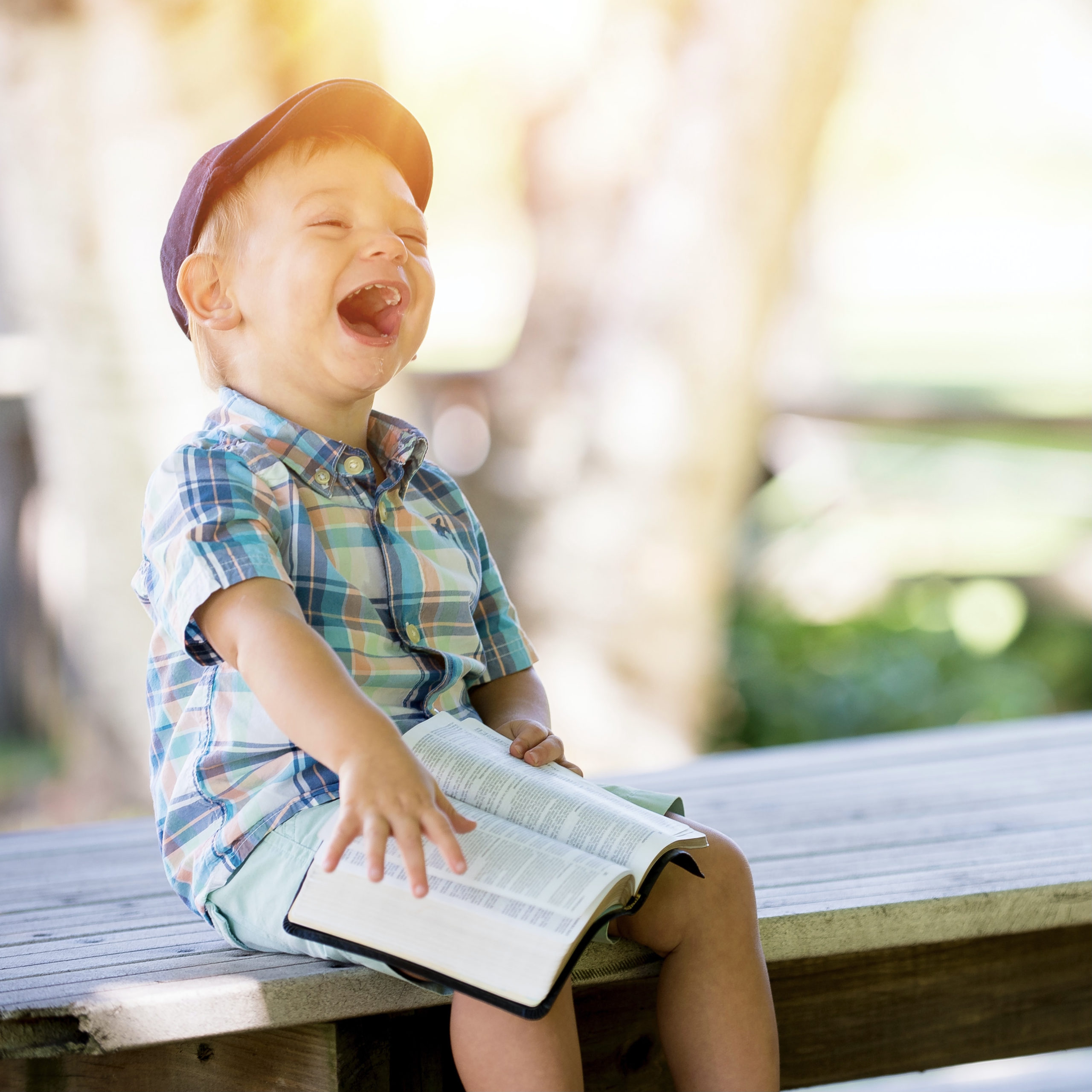 difference between happiness and joy | toddler sitting on a bench, holding a bible, and laughing hard