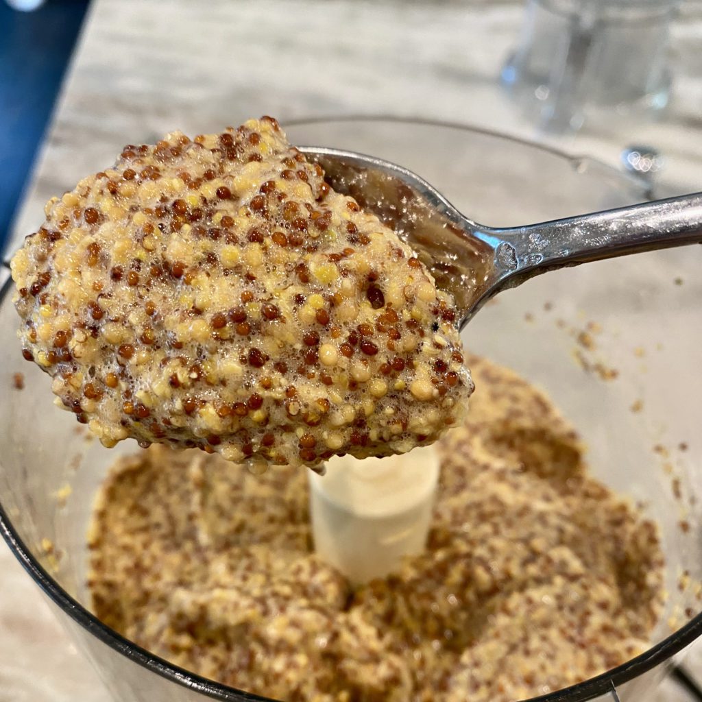 all of the ingredients in a food processor. Some is scooped out on a spoon | whole grain mustard recipe | Positively Jane  