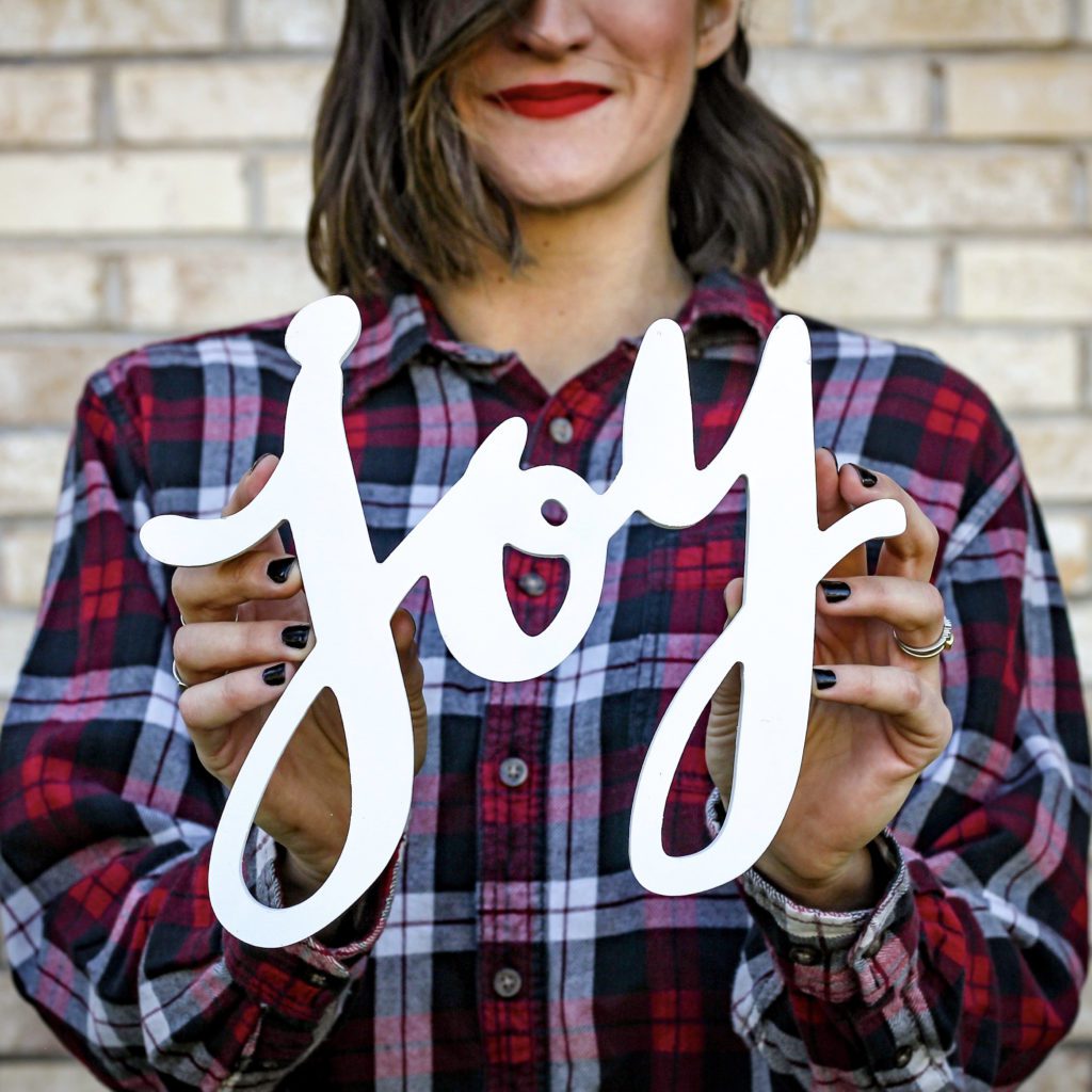 girl with long dark hair, dressed in a plaid shirt, holding onto the word joy | reclaim your  joy | Positively Jane.j