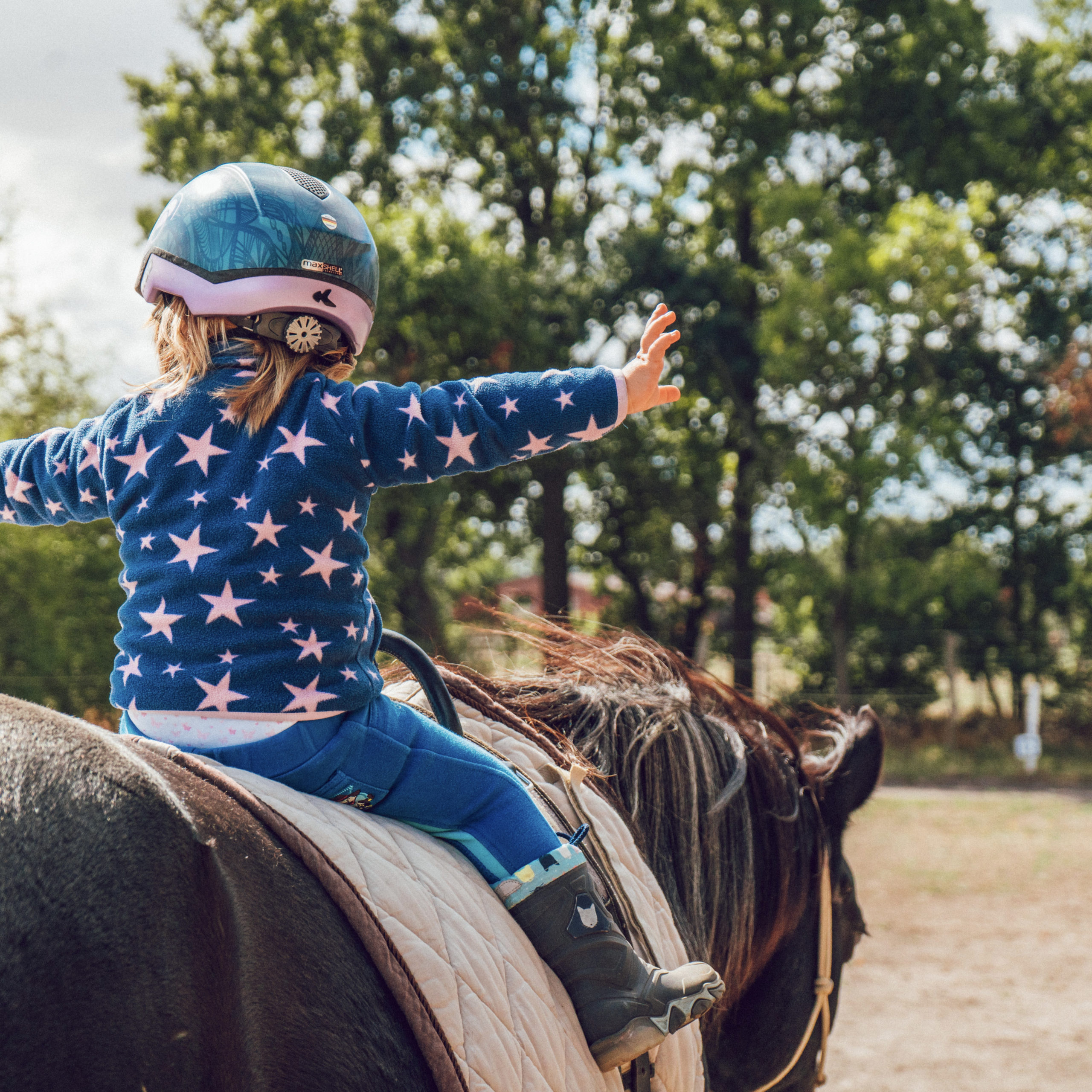 3 year old girl riding a horse without a harness. She is wearing blue sweatshirt with white stars and a stars and stripes helmet. She looks like a super hero. | are you letting fear lead your life | Positively Jane