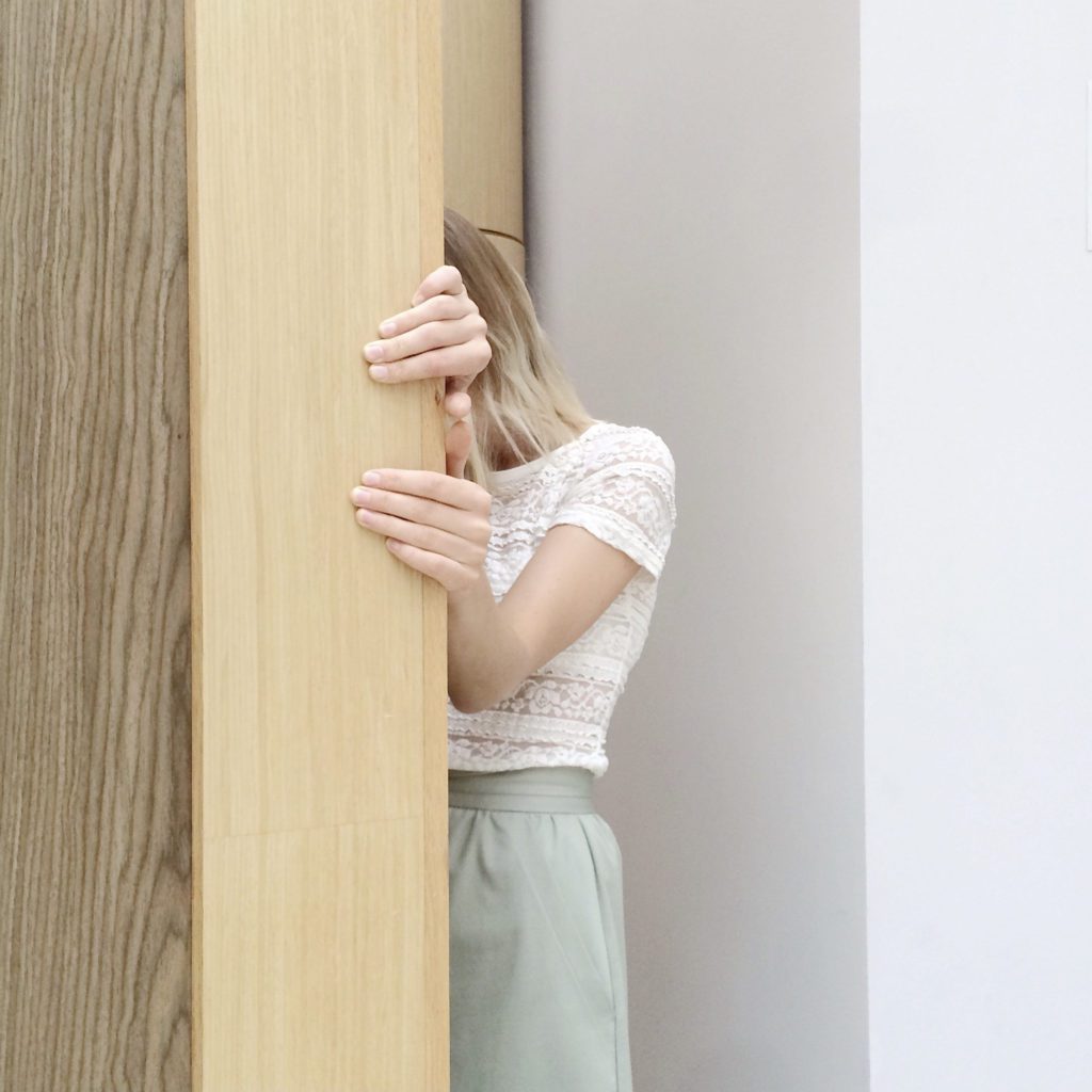 woman with a white shirt and green skirt hiding behind a wall | are you letting fear lead your life