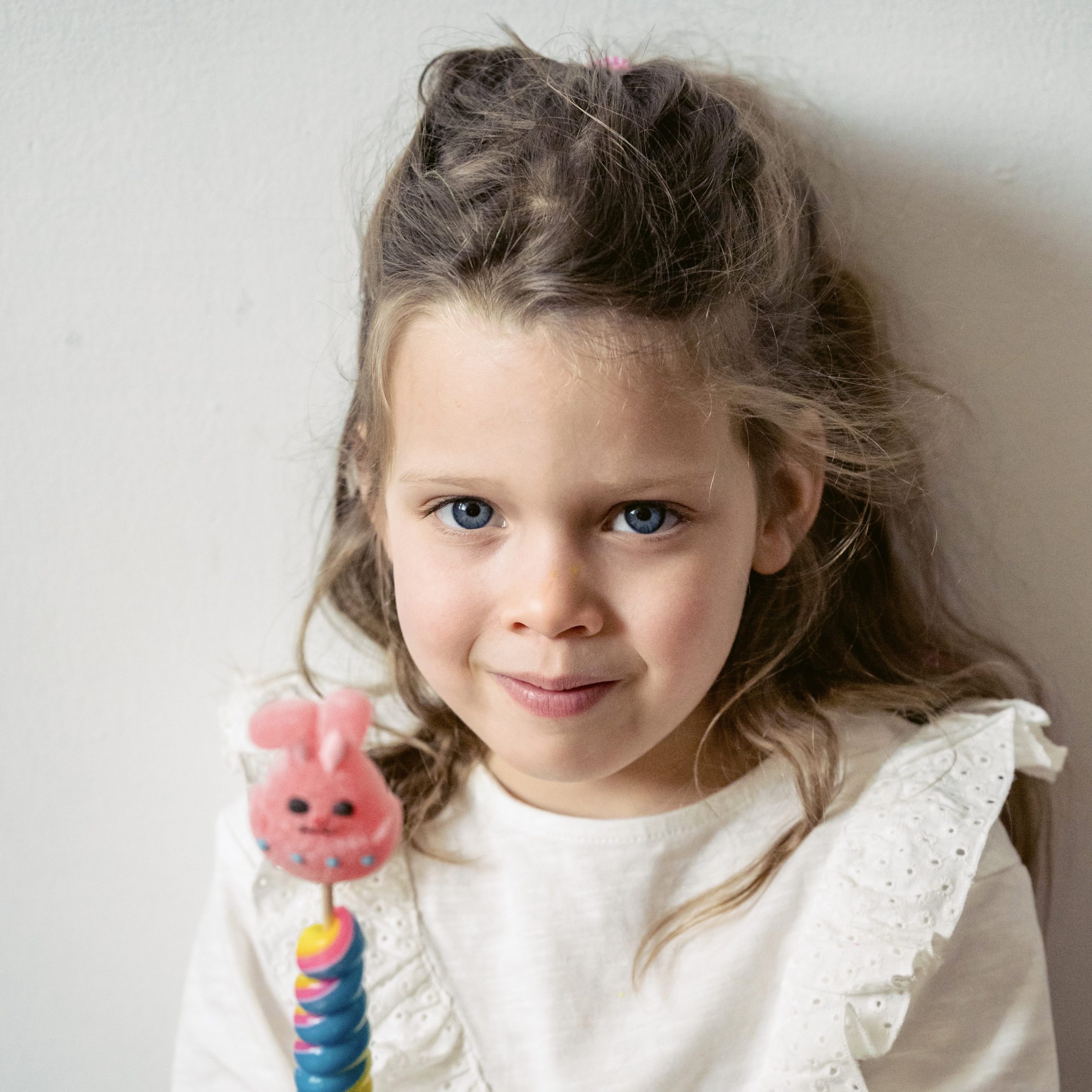 little girl wearing white and holding a stick with a pink bunny on tip | kids and budgets | Positively Jane