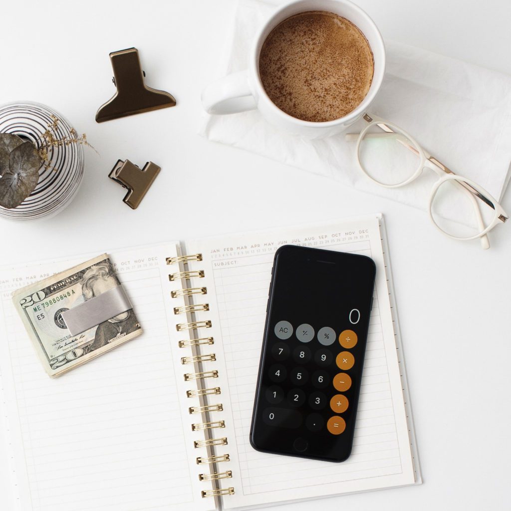 calculator, coffee, money and a notebook on a desk | 3 financial mistakes most women make | positively jane