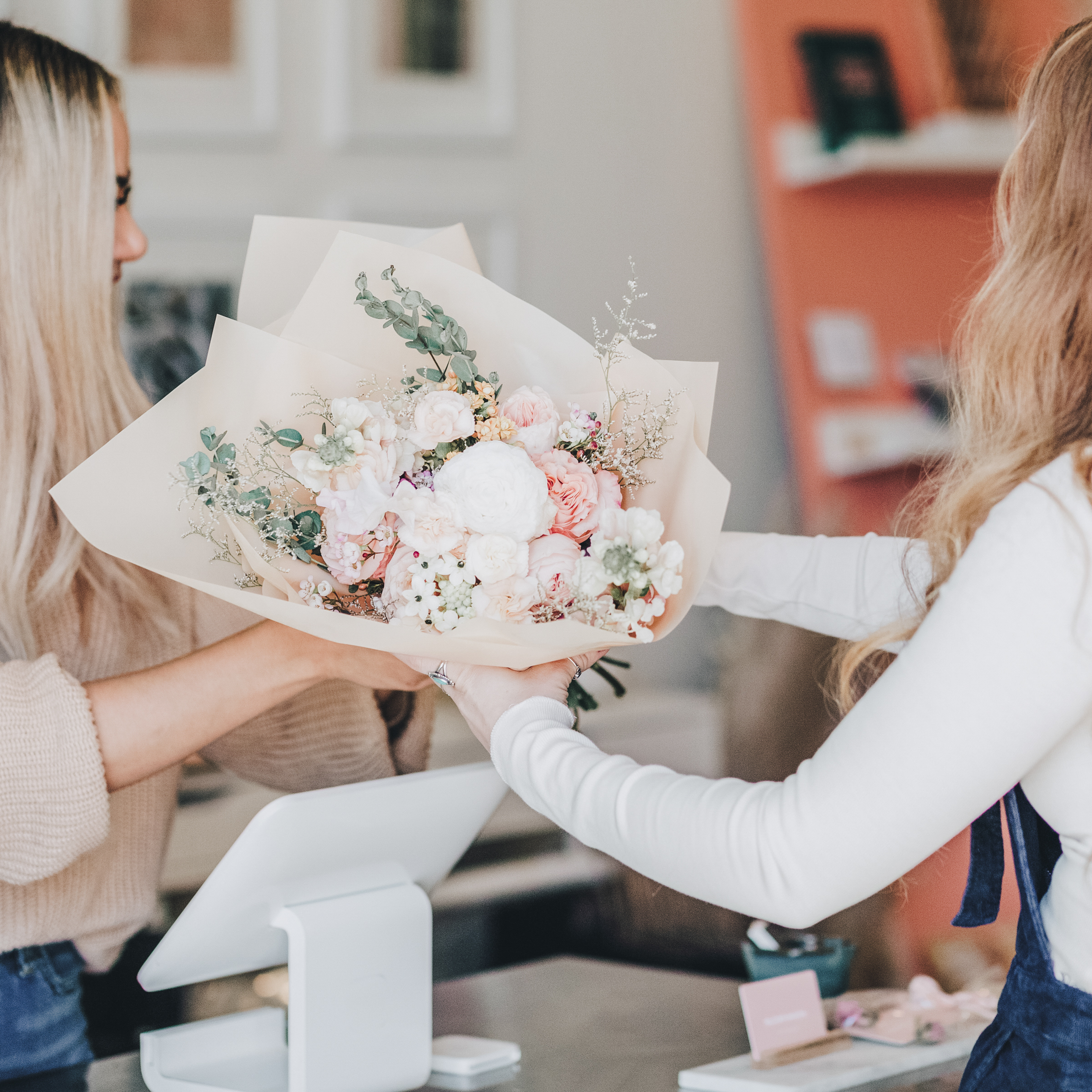 women in white handing a bouquet of flowers to another woman in a store | create financial independent | positively jane