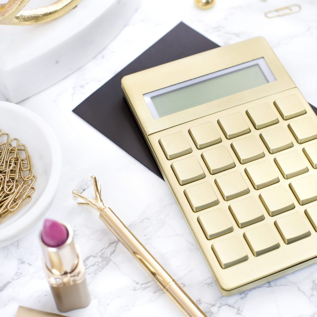 gold calculator on a white desk | 5 ways to get ahead financially | Positively Jane  